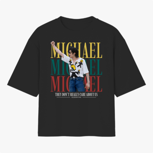Camiseta com estampa frontal de um artista performando, sobreposta a três repetições do nome "Michael" em amarelo, verde e vermelho, acompanhada da frase "They Don't Really Care About Us".