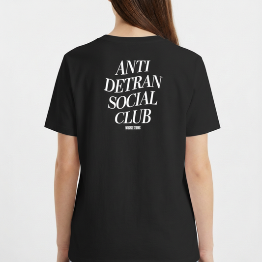 Camiseta com estampa frontal de escrita "ANTI DETRAN SOCIAL CLUB" e estampa traseira maior com a mesma mensagem, acompanhada por "NO BREAK STUDIOS".