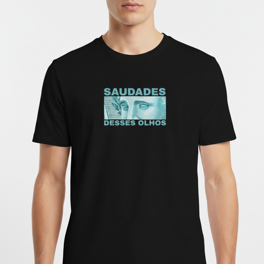 Camiseta com estampa frontal de ilustração de rosto de estátua com olhos destacados, ladeado por texto "SAUDADES DESSES OLHOS" em letras maiúsculas.