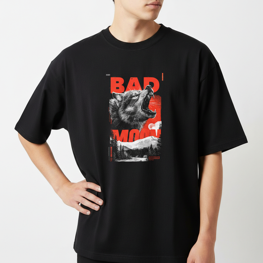 Camiseta com estampa frontal de um lobo uivante sobreposto a letras maiúsculas "BAD MOON", em contraste com uma paisagem de floresta ao fundo.