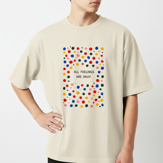 Camiseta com estampa frontal de padrão de bolinhas coloridas ao redor da frase central "ALL FEELINGS ARE OKAY", criando um visual vibrante e acolhedor.