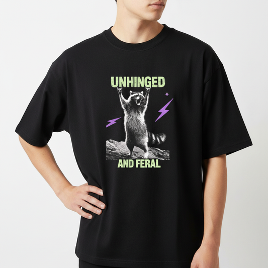 Camiseta com estampa frontal de guaxinim em pose exuberante entre raios estilizados, acompanhada das palavras "Unhinged" e "And Feral" em fonte marcante.