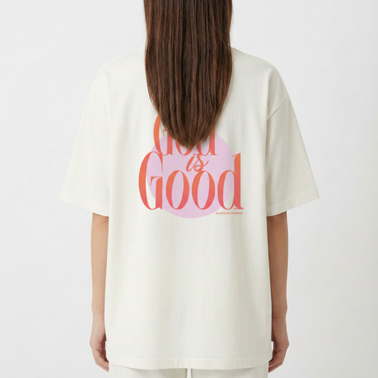 Camiseta com estampa frontal de "lab" em letras vibrantes e detalhes de linhas onduladas, e estampa traseira de "God is Good" sobrepondo um círculo.