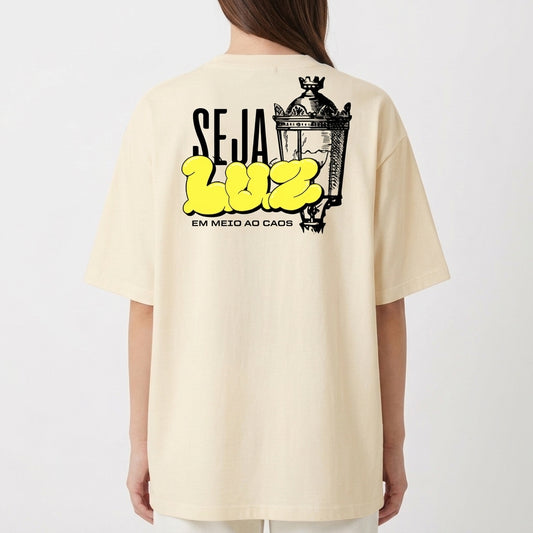 Camiseta com estampa frontal de texto estilizado com as palavras "RLEM Company" e estampa traseira de lâmpada vintage acompanhada da frase "SEJA LUZ EM MEIO AO CAOS".
