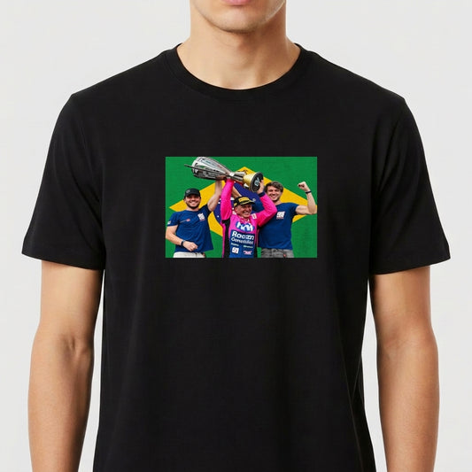 Camiseta com estampa frontal de três pessoas celebrando com um troféu acima de suas cabeças, em frente a uma bandeira estilizada ao fundo.