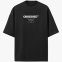 Camiseta com estampa frontal de texto grande "OBSESSED" e abaixo uma sequência de textos menores combinando palavras e símbolos minimalistas.