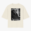 Camiseta com estampa frontal de fotografia em preto e branco de uma pessoa usando óculos escuros, com texto estilizado acima e abaixo da imagem.