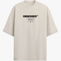 Camiseta com estampa frontal de texto grande "OBSESSED" e abaixo uma sequência de textos menores combinando palavras e símbolos minimalistas.