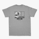 Camiseta com estampa traseira de onda dividida em três painéis, acompanhada do texto "TOKYO 1986" e caracteres japoneses abaixo.