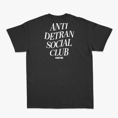 Camiseta com estampa frontal de escrita "ANTI DETRAN SOCIAL CLUB" e estampa traseira maior com a mesma mensagem, acompanhada por "NO BREAK STUDIOS".
