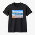 Camiseta com estampa frontal de uma praia com barcos no horizonte e uma criança na areia, e estampa traseira com a inscrição "PITANGUI-RN".