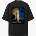 Camiseta com estampa frontal de logotipo minimalista e estampa traseira de prancha de surf encostada em parede desgastada com palmeira e fundo geométrico.