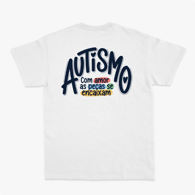 Camiseta com estampa frontal de mãos formando coração com peças de quebra-cabeça coloridas e estampa traseira com frase sobre autismo em diferentes cores.