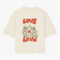 Camiseta com estampa frontal de dois esqueletos encarando-se carinhosamente, cercados pela frase "LOVE IS LOVE" em letras estilizadas e destacadas.