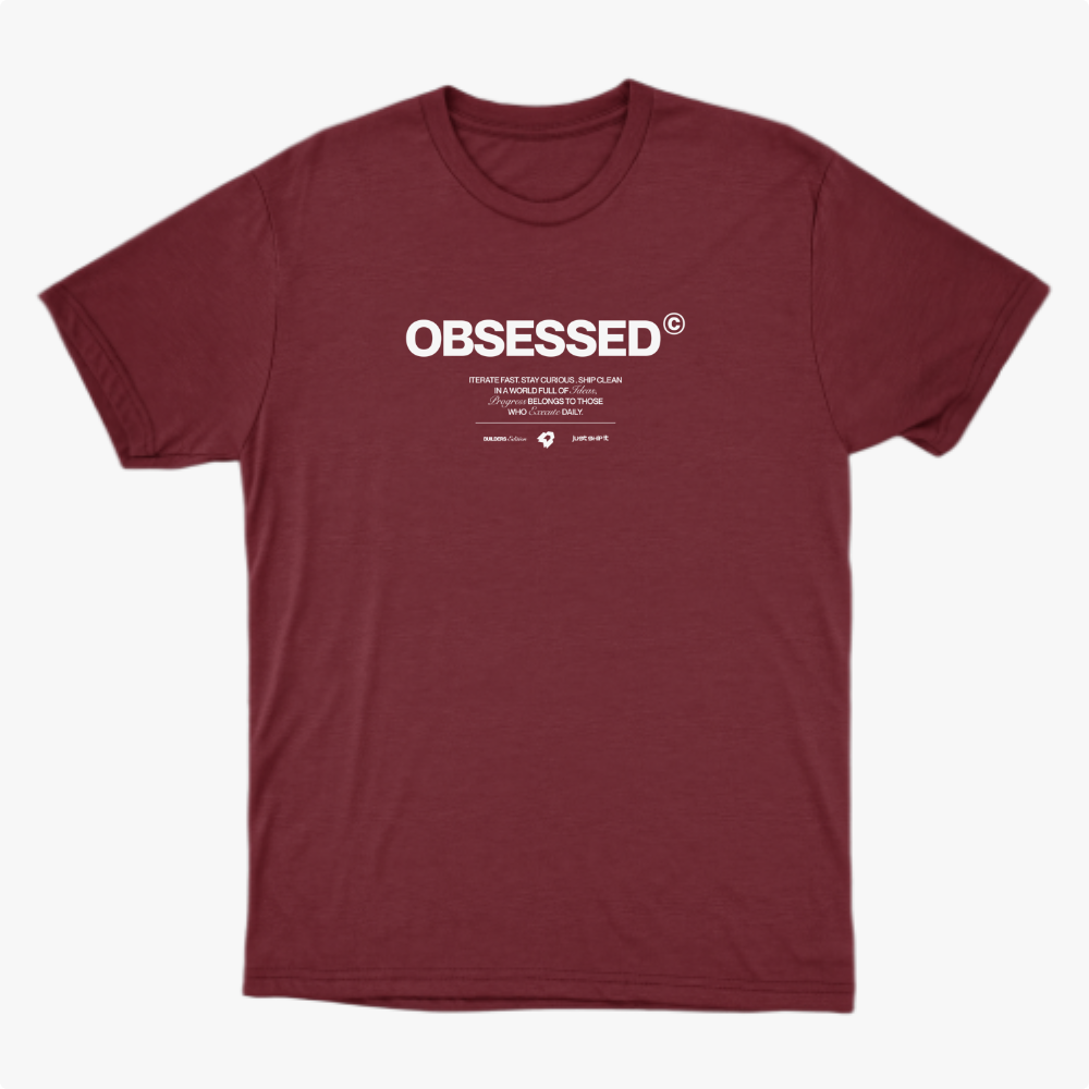 Camiseta com estampa frontal de texto grande "OBSESSED" seguido por linhas menores que incluem mensagens inspiradoras e dois logotipos pequenos abaixo.