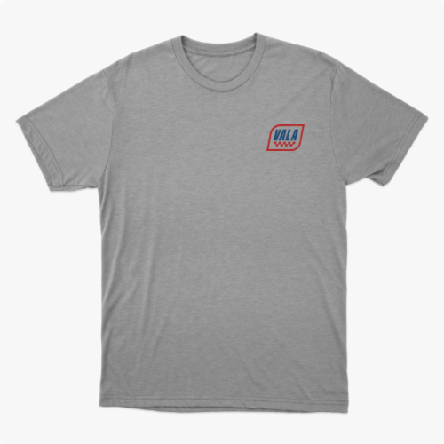 Camiseta com estampa frontal de um emblema pequeno com a palavra "VALA" e estampa traseira com texto "VALA KUSTOM SEM DESCULPAS SEM REMORSOS" e detalhes geométricos.