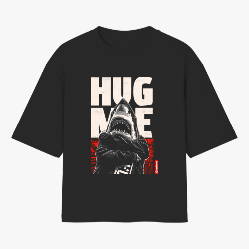 Camiseta com estampa frontal de tubarão antropomorfizado de braços cruzados, sobreposto a letras grandes "HUG ME" e fundo abstrato geométrico.