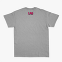 Camiseta com estampa frontal de cruz contendo a frase "Lugar abençoado" e símbolo decorativo, e estampa traseira de texto "LAB" em destaque.