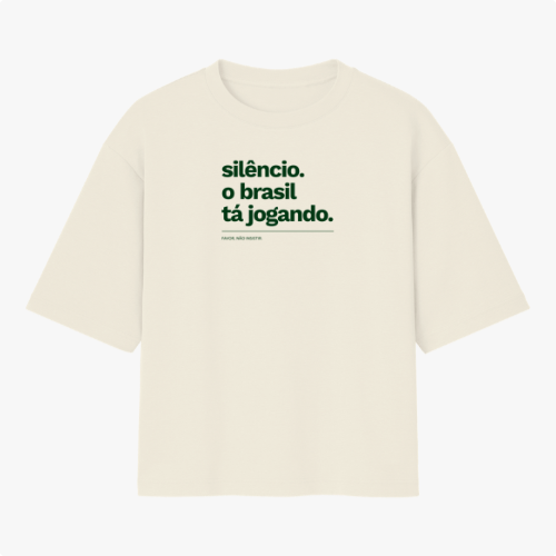 Camiseta com estampa frontal de texto "silêncio. o brasil tá jogando." com assinatura "FALAR, NÃO MURMURAR." e estampa traseira de "VERDELO" no topo.