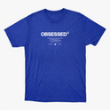 Camiseta com estampa frontal de texto grande "OBSESSED" seguido por linhas menores que incluem mensagens inspiradoras e dois logotipos pequenos abaixo.