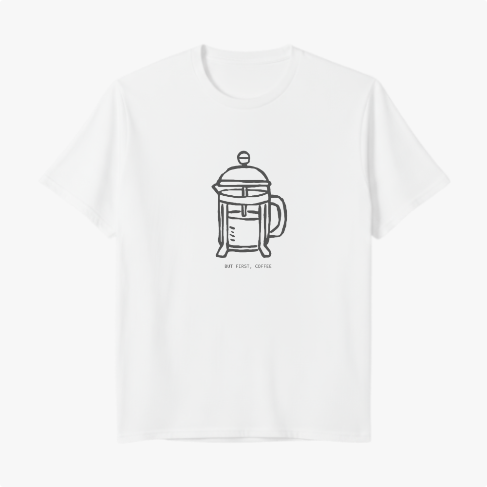 Camiseta com estampa frontal de cafeteira tipo prensa francesa desenhada de forma minimalista, acompanhada da frase "BUT FIRST, COFFEE" em letras discretas.