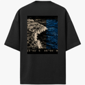 Camiseta com estampa frontal de símbolo minimalista em forma de flecha e estampa traseira de fotografia de oceano com coordenadas no rodapé.