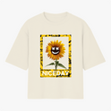 Camiseta com estampa frontal de girassol estilizado com sorriso, cercado por moldura amarela com padrões gráficos e texto "NICE DAY" em destaque.