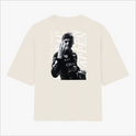Camiseta com estampa frontal de um logotipo e nome em tamanho pequeno e estampa traseira de um piloto em ação com texto estilizado ao fundo.