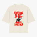 Camiseta com estampa frontal de um urso sobre blocos de construção com a frase em destaque "Trying to Get My Shit Together" em letras estilizadas.