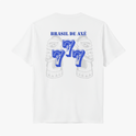 Camiseta com estampa frontal de brasão detalhado e estampa traseira de "Brasil de Axé" com números "777" estilizados sobre imagem difusa de elementos culturais.