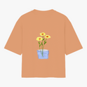 Camiseta com estampa frontal de texto em letras simples "Il raccolto è inevitabile." e estampa traseira de vaso azul com três flores amarelas e caule verde.