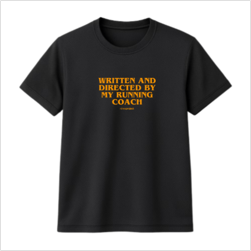 Camiseta com estampa frontal de texto que diz "WRITTEN AND DIRECTED BY MY RUNNING COACH" acompanhado de um pequeno logo ou assinatura abaixo.
