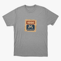 Camiseta com estampa frontal de um selo retangular retrô com o ano "1986" no topo e a inscrição "Rede Manchete" abaixo, separado por um símbolo estilizado.
