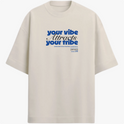 Camiseta com estampa frontal de texto estilizado "your vibe attracts your tribe" em letras grandes, acompanhada de pequenos detalhes textuais complementares.