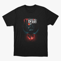 Camiseta com estampa frontal de texto "Welcome to Derry" acima de um balão flutuante, com silhuetas refletidas em um fundo iluminado.