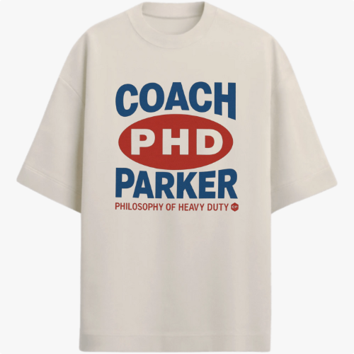 Camiseta com estampa frontal de texto estilizado com palavras "COACH PHD PARKER" em destaque, acompanhada de "PHILOSOPHY OF HEAVY DUTY" em menor tamanho.