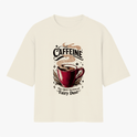 Camiseta com estampa frontal de uma xícara de café com vapor, rodeada por estrelas, a palavra "CAFFEINE" acima e a frase "The Adult Version of Fairy Dust" abaixo.