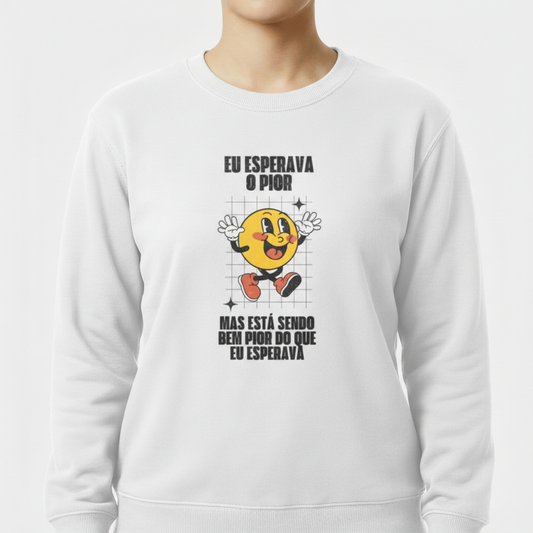 Moletom com estampa frontal de uma face sorridente com luvas e sapatos, cercada por grade sutil, acompanhada pela frase "Eu esperava o pior, mas está sendo bem pior do que eu esperava".