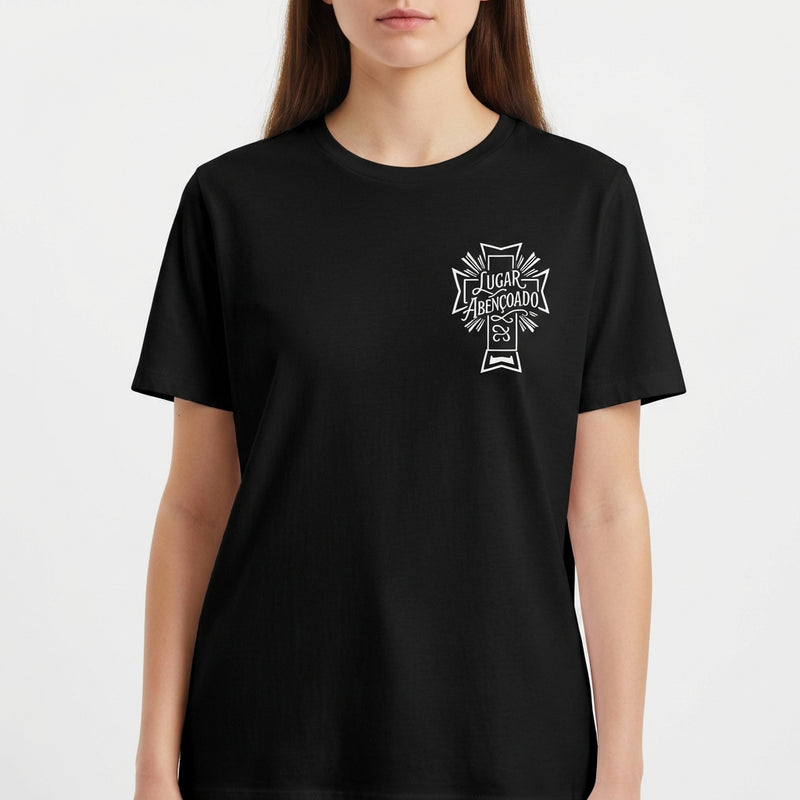 Camiseta com estampa frontal de cruz contendo a frase "Lugar abençoado" e símbolo decorativo, e estampa traseira de texto "LAB" em destaque.