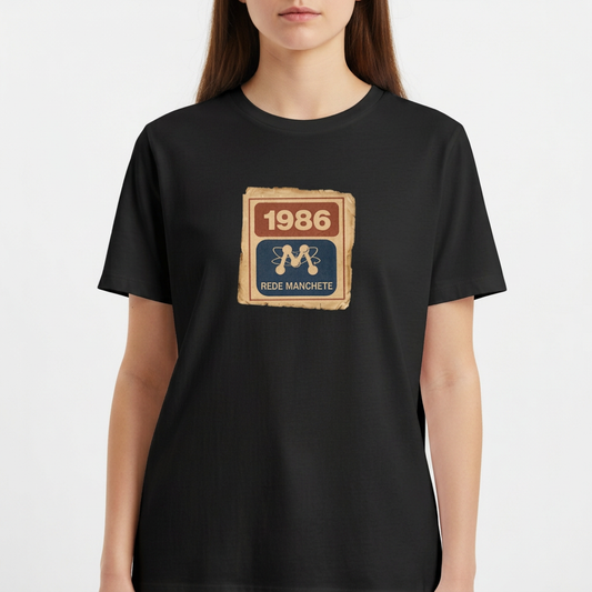 Camiseta com estampa frontal de um selo retangular retrô com o ano "1986" no topo e a inscrição "Rede Manchete" abaixo, separado por um símbolo estilizado.