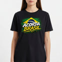 Camiseta com estampa frontal de bandeira estilizada, com o texto "ACORDA BRASIL" em destaque sobre um fundo pincelado e cinco estrelas alinhadas.