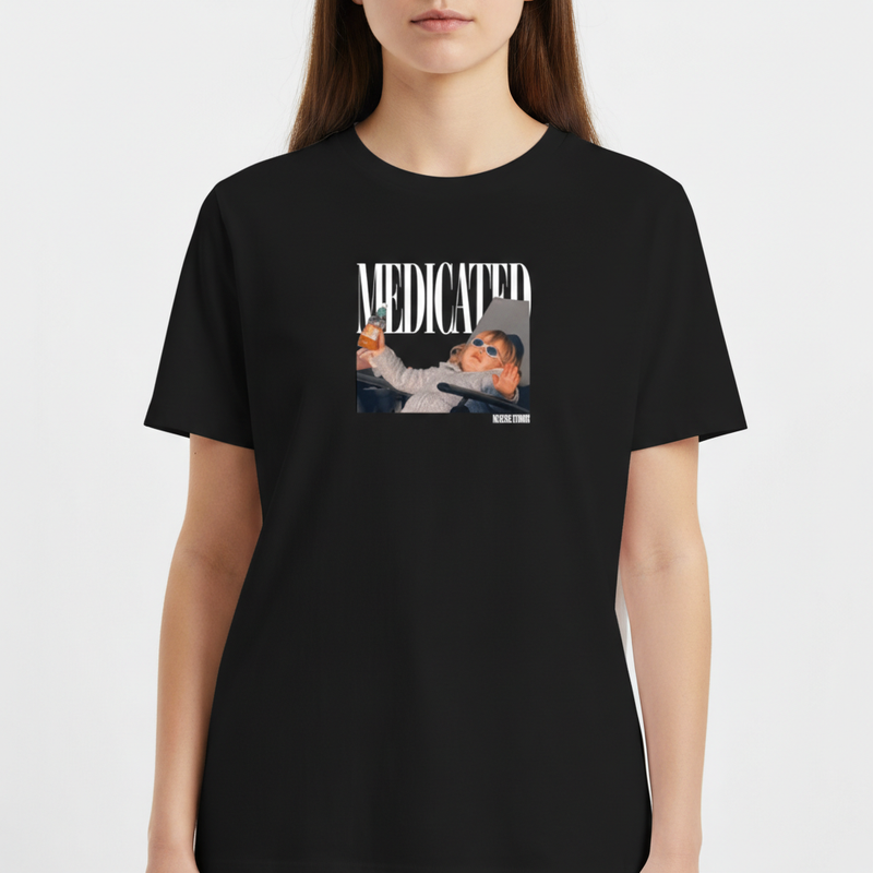 Camiseta com estampa frontal de fotografia de bebê com óculos escuros segurando uma mamadeira, acompanhada da palavra "MEDICATED" em letras grandes.