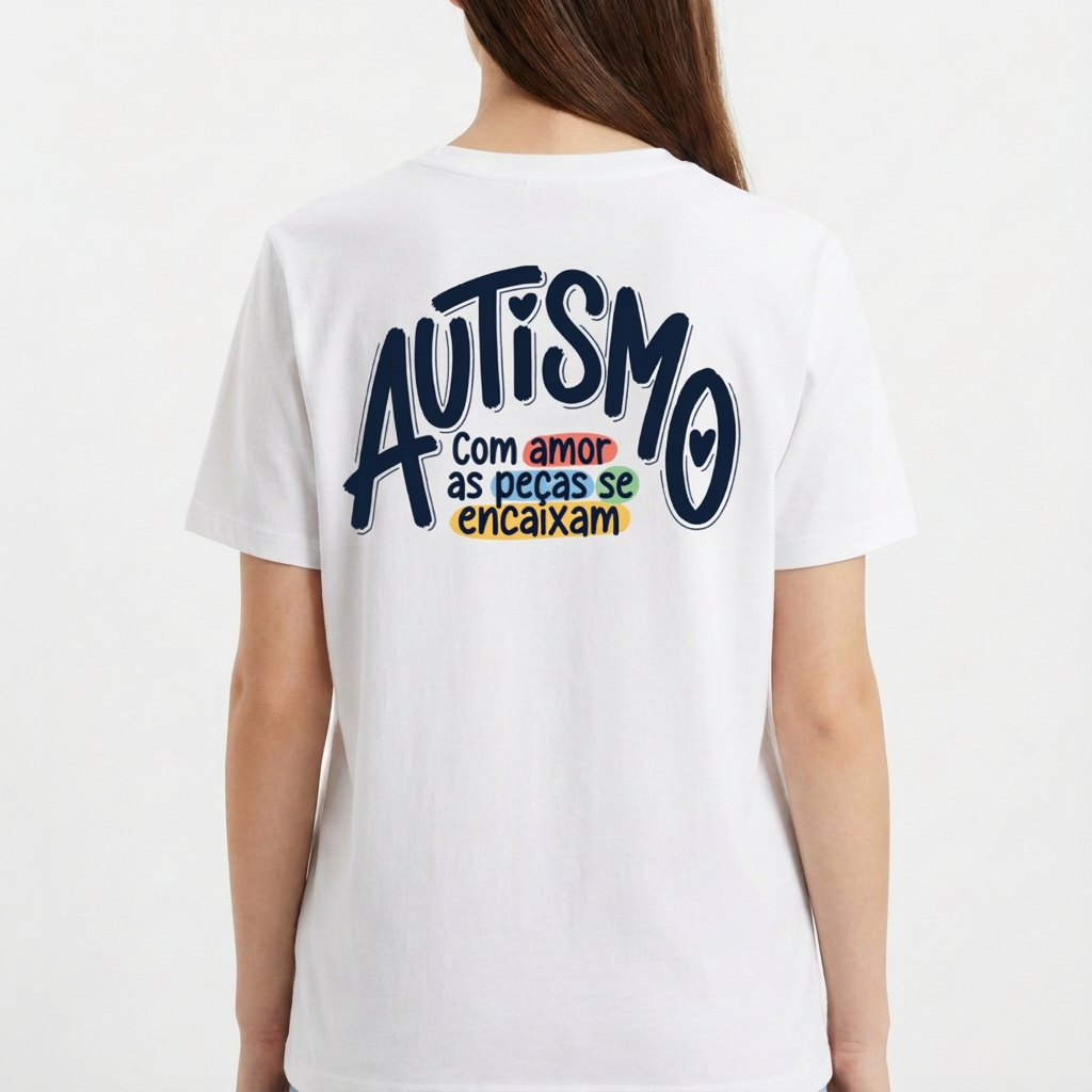 Camiseta com estampa frontal de mãos formando coração com peças de quebra-cabeça coloridas e estampa traseira com frase sobre autismo em diferentes cores.