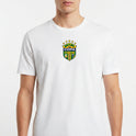 Camiseta com estampa frontal de brasão com cinco estrelas acima e frases "BRASIL NA COPA" e "E NÓS NO SOFÁ", acompanhado de duas bandeiras na lateral.