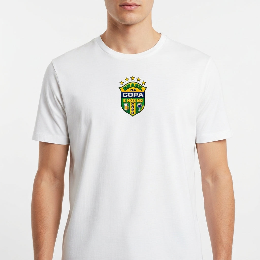 Camiseta com estampa frontal de brasão com cinco estrelas acima e frases "BRASIL NA COPA" e "E NÓS NO SOFÁ", acompanhado de duas bandeiras na lateral.