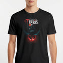 Camiseta com estampa frontal de texto "Welcome to Derry" acima de um balão flutuante, com silhuetas refletidas em um fundo iluminado.