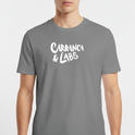 Camiseta com estampa frontal de letras estilizadas "Carranca & Labs" e estampa traseira de um desenho gráfico de figura caricata com expressão marcante.