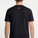 Camiseta com estampa frontal de cruz contendo a frase "Lugar abençoado" e símbolo decorativo, e estampa traseira de texto "LAB" em destaque.