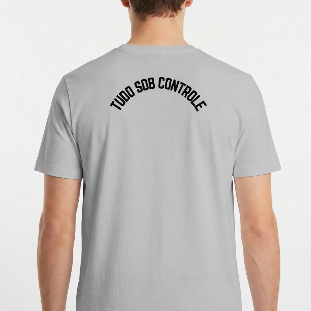 Camiseta com estampa frontal de gato preto segurando um copo, envolto em formas abstratas, e estampa traseira com texto em arco "TUDO SOB CONTROLE".