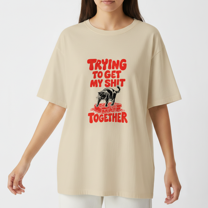 Camiseta com estampa frontal de um urso sobre blocos de construção com a frase em destaque "Trying to Get My Shit Together" em letras estilizadas.
